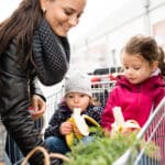 parents pushing shopping cart with groceries and their daughters