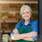 portrait of confident owner with arms crossed standing in small grocery store