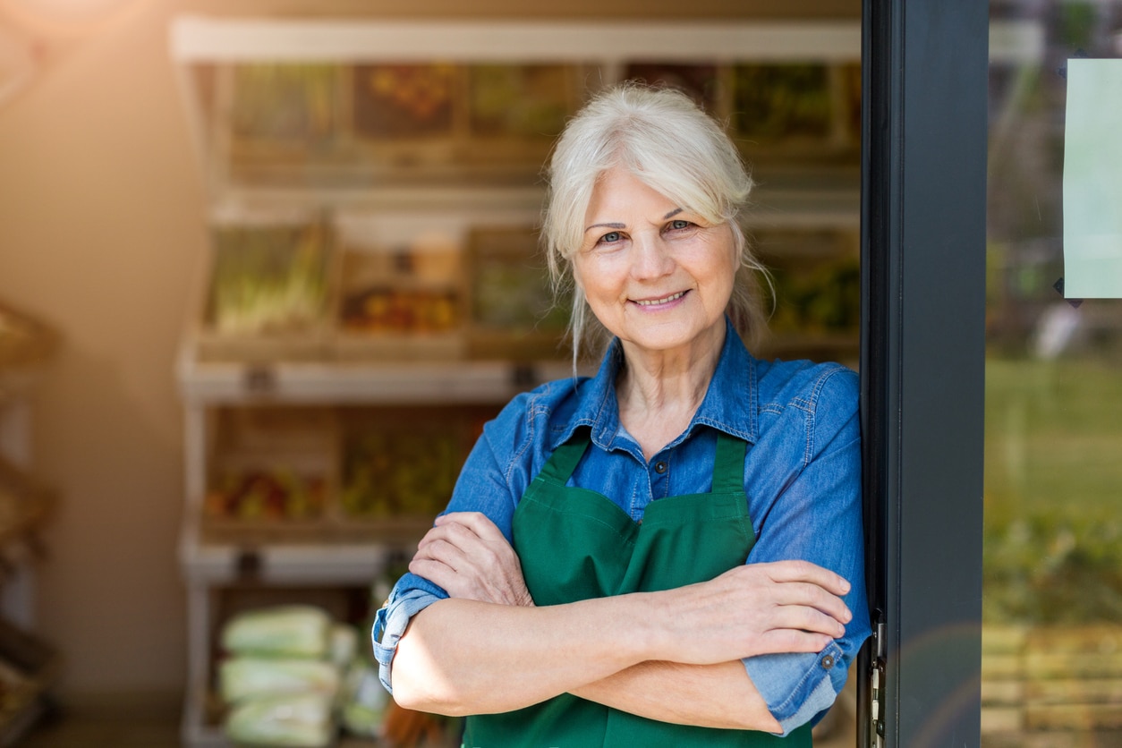 portrait of confident owner with arms crossed standing in small grocery store