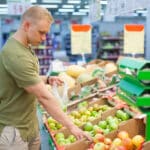 young sporty man is choosing fruits in grocery store. concept of healthy nutrition, balanced diet, vitamins